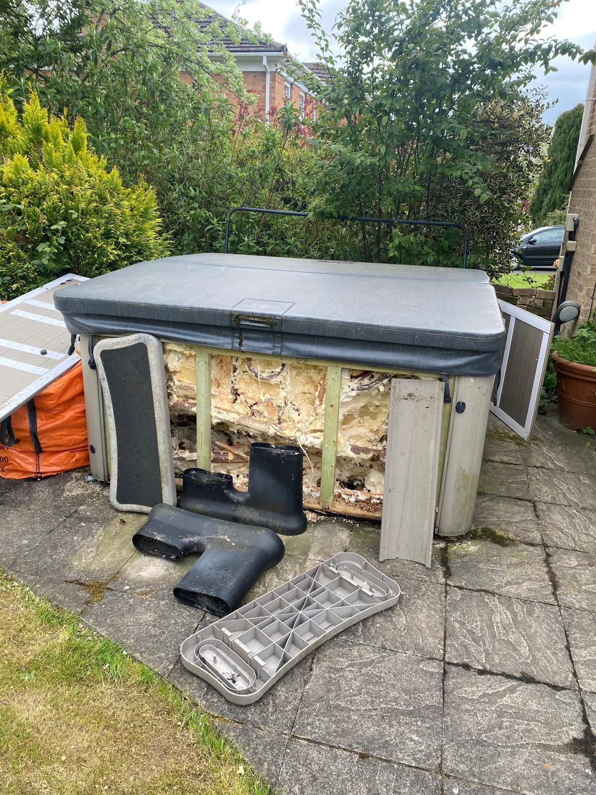 Weathered outdoor hot tub with gray cover and detached skirt panels on garden patio